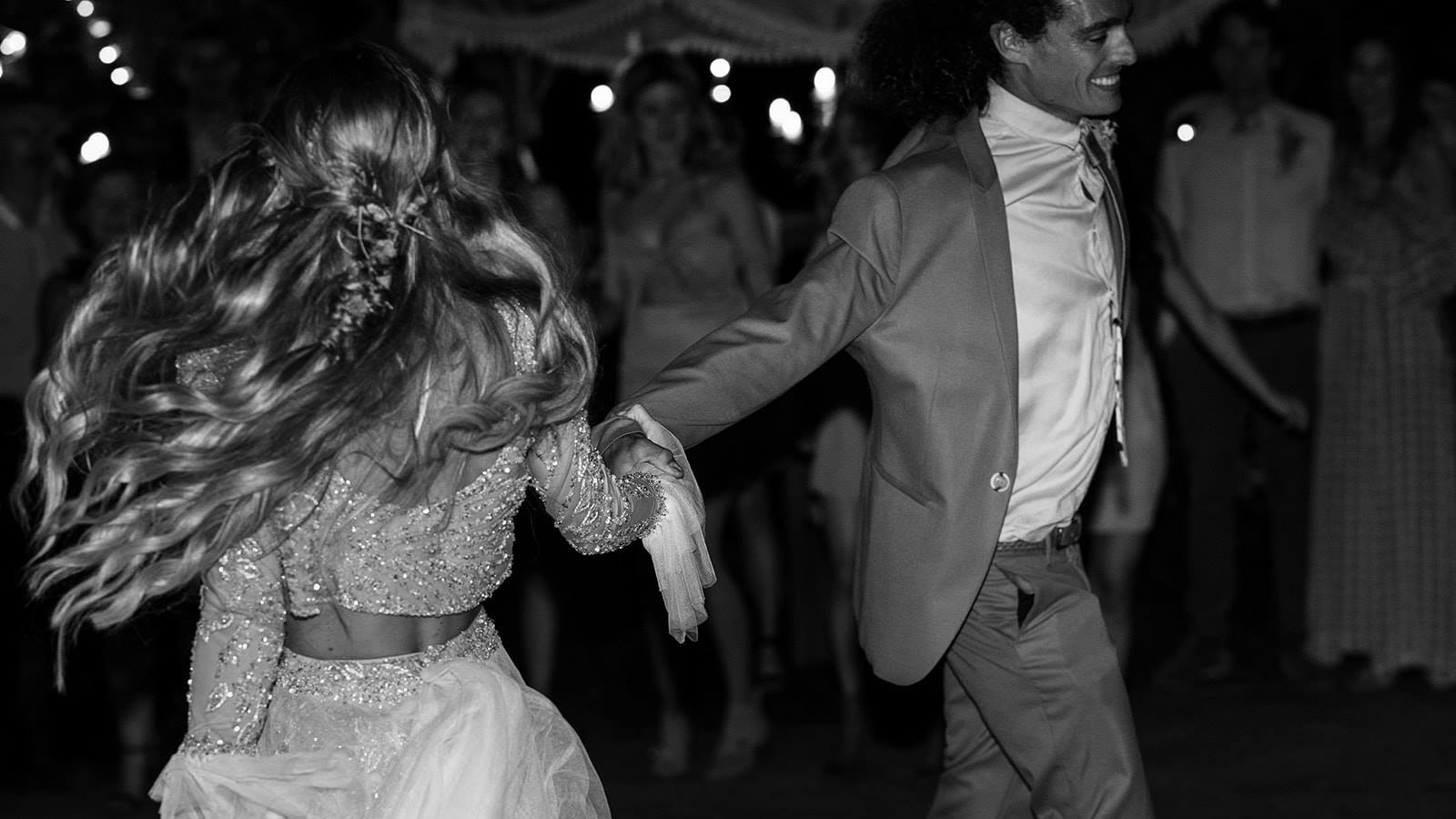 Bride and groom dancing together at an outdoor evening wedding reception with string lights overhead